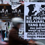 Sejumlah pengendara melintas di dekat poster himbauan bertuliskan "Ke Jogja Belajarlah Yang Baik dan Jadilah Warga Yang Baik, Jogja Nyaman Tanpa Preman" yang terpasang di jalan Cendana, Yogyakarta, Minggu (1/4).